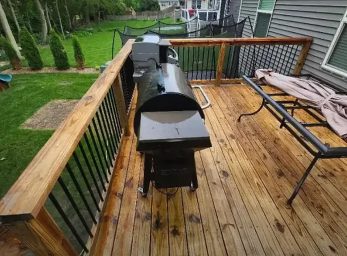 Wooden back deck with a grill and a bench beside a house