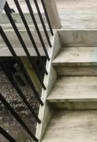 Grey mossy wooden stair treads with a black metal railing