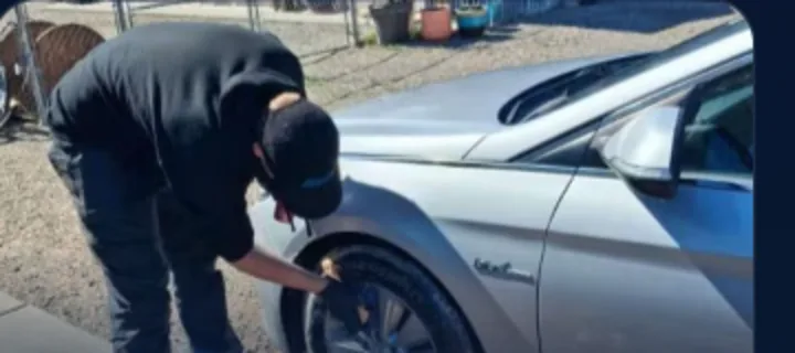 Detailer in a black hoodie scrubbing a dirty silver car wheel